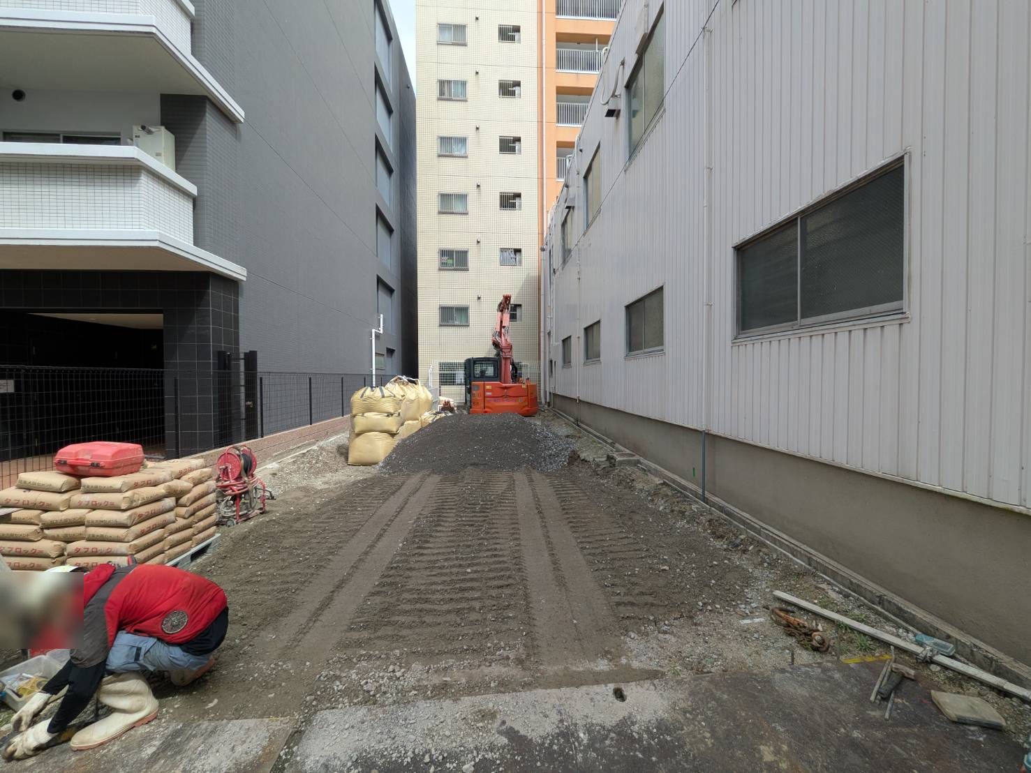 セメント系固化材（袋）を搬入し、小型バックホウで土と混合。間口の狭い敷地に合わせた機械の選定です。